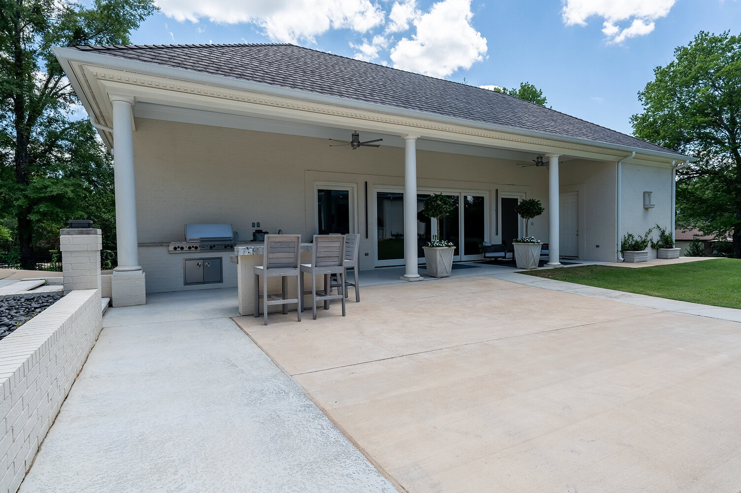 Spacious outdoor patio with grill, dining table, and potted plants under a covered area.