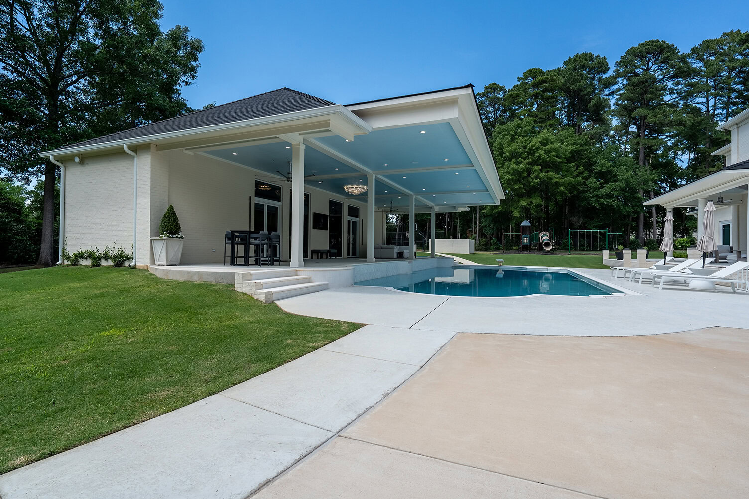 Contemporary backyard with pool, covered patio, and lush greenery.