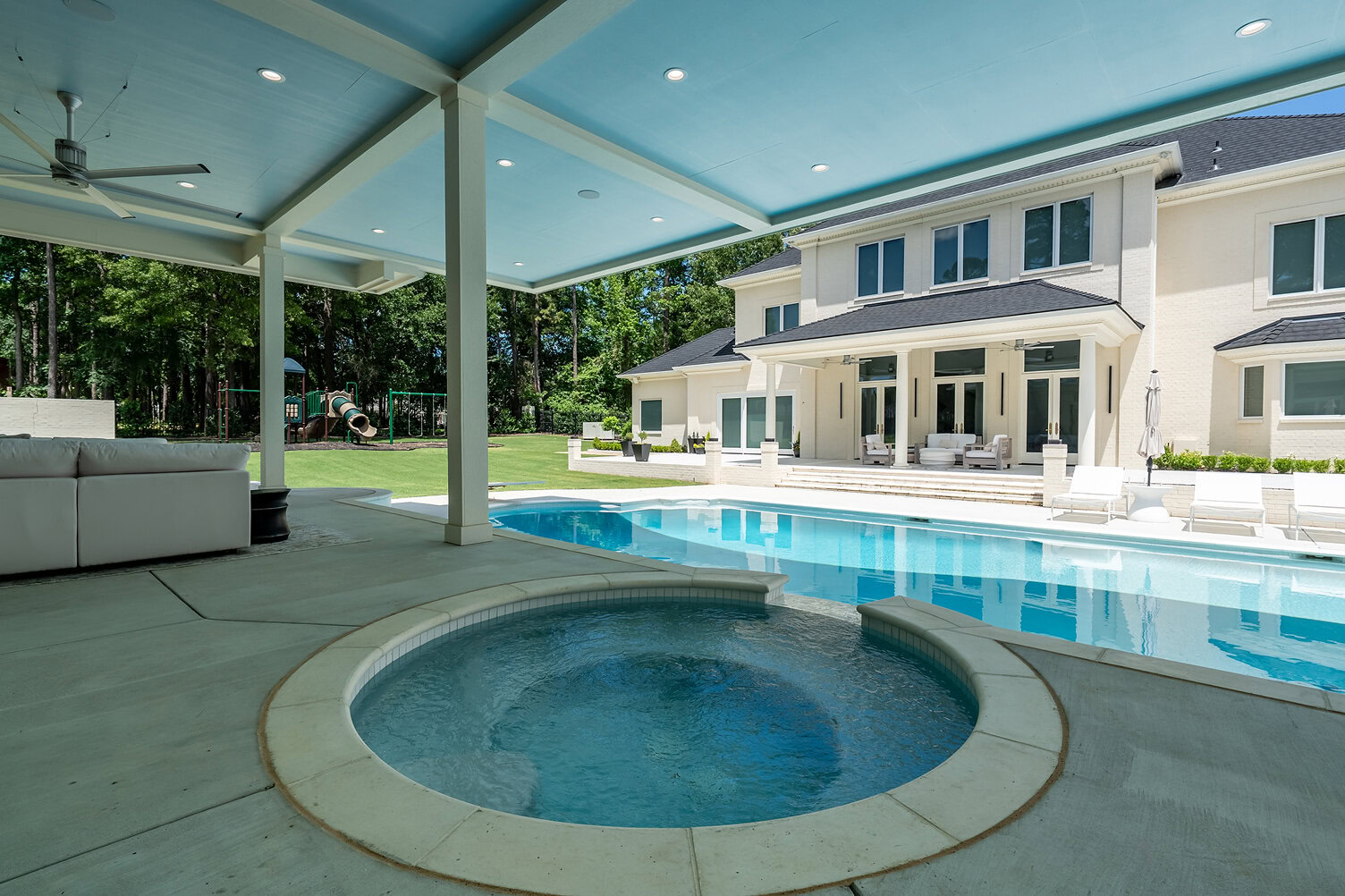 Modern backyard with swimming pool, hot tub, and covered patio area.
