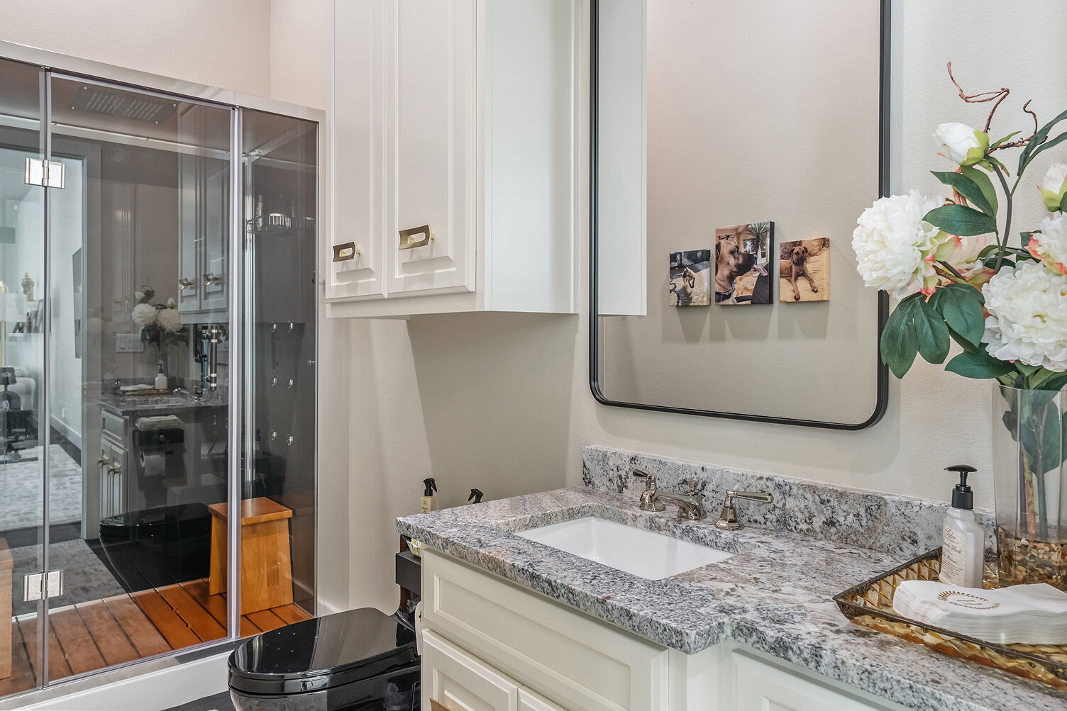 Bright bathroom with white cabinets, granite countertop, and floral decor.