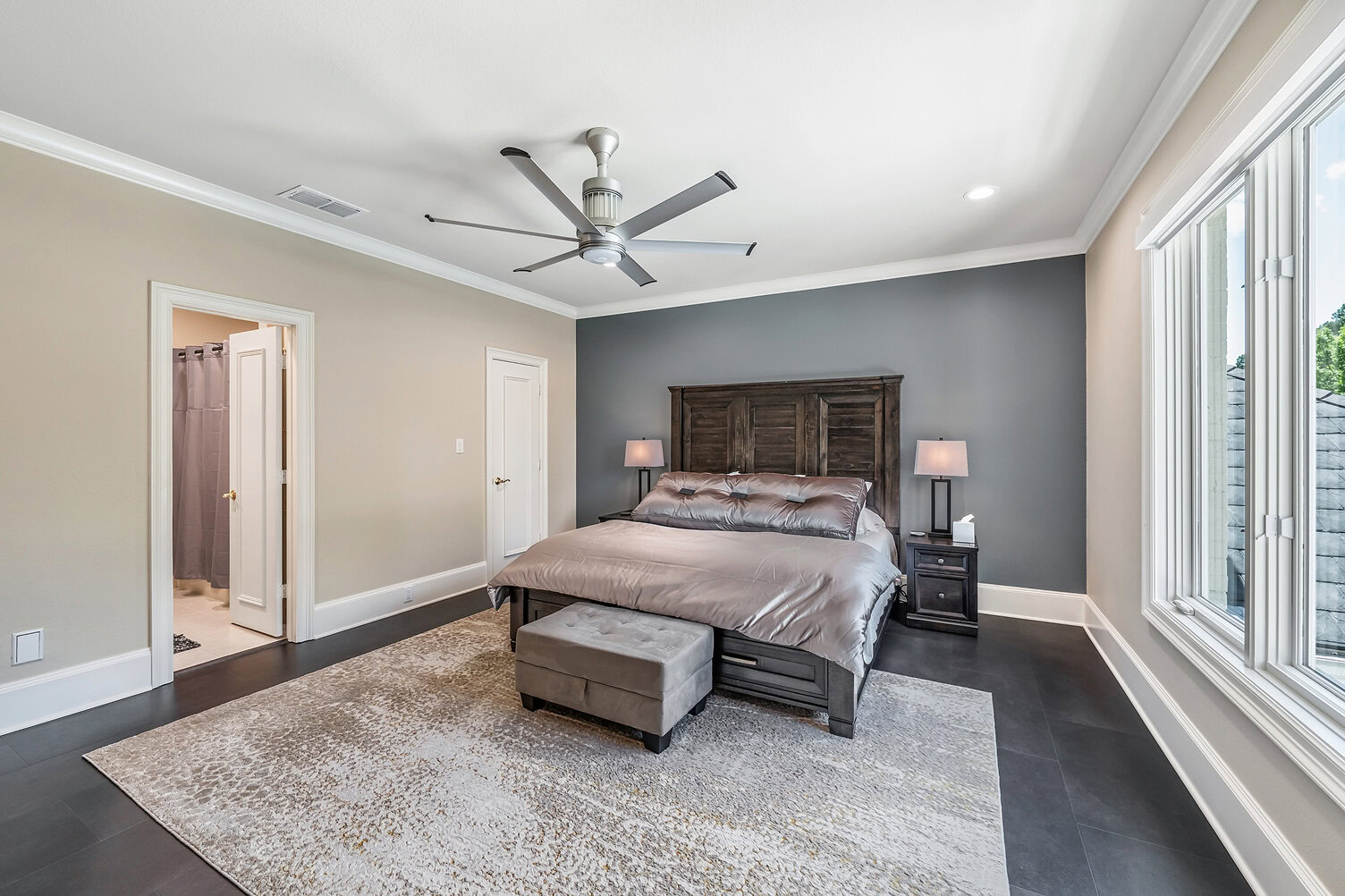 Spacious bedroom with large windows, dark wood furniture, and neutral decor.