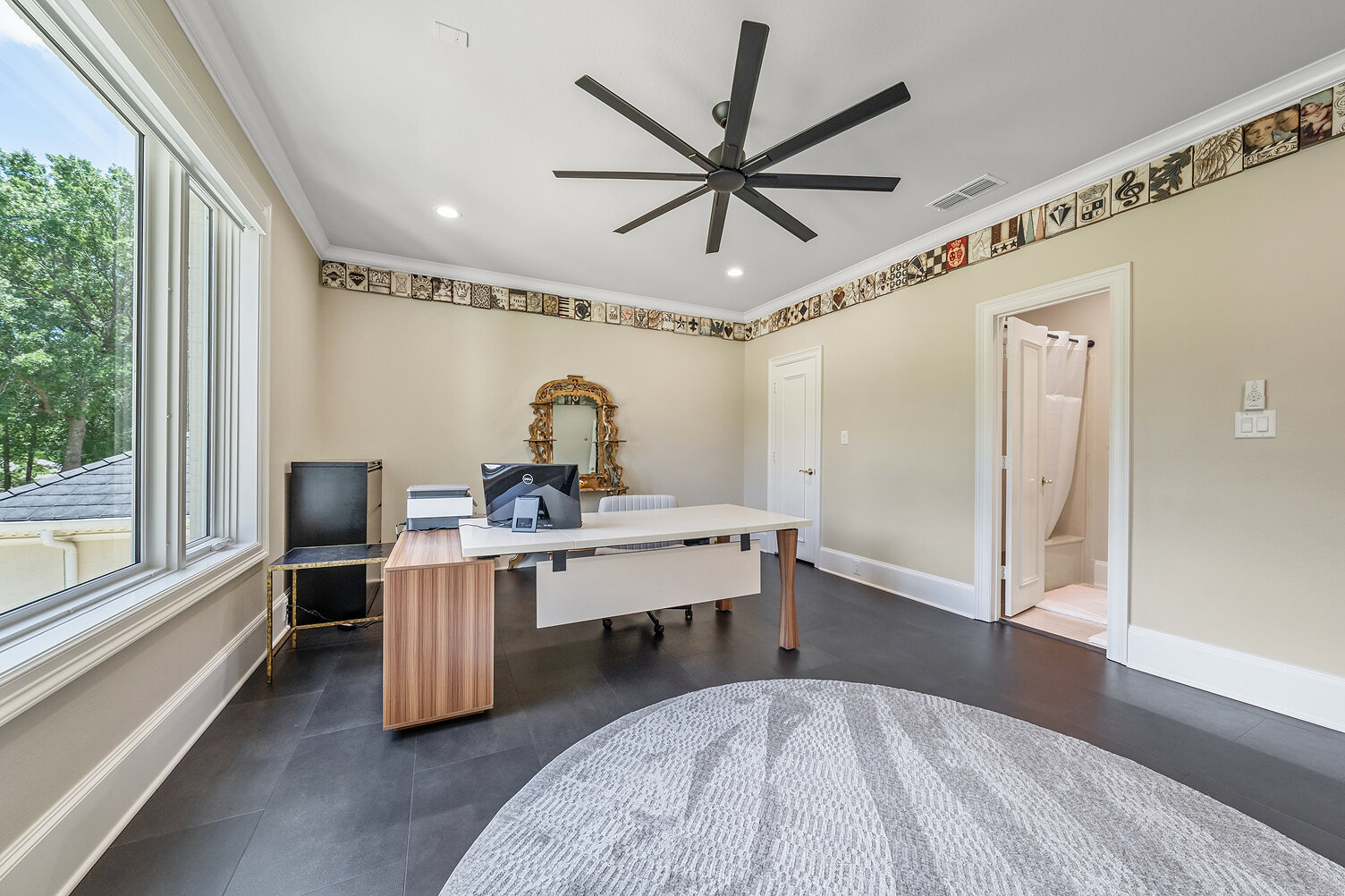 Spacious office with large window, modern ceiling fan, and neutral decor.