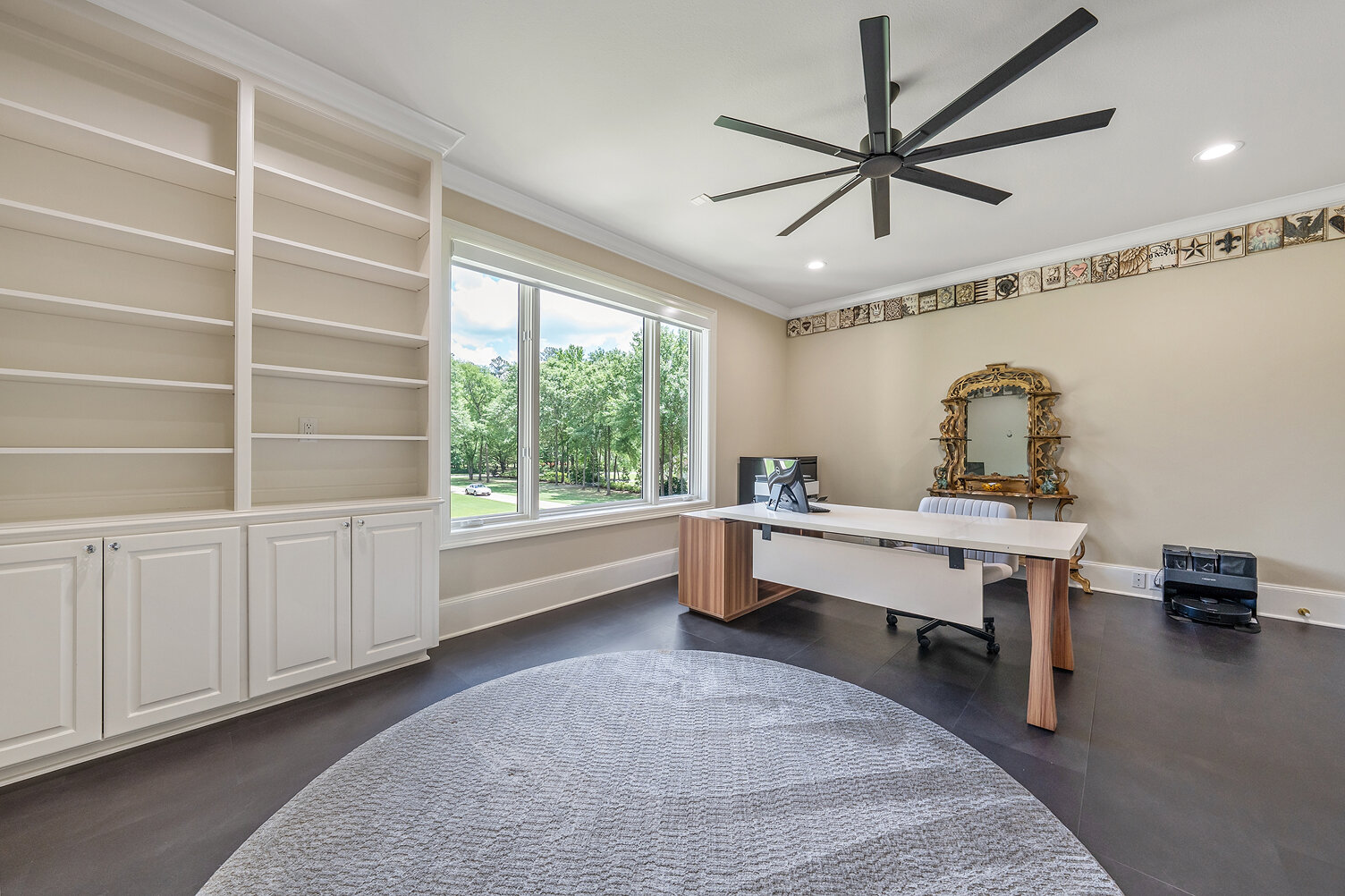 Bright home office with large window, white shelves, and a desk with a mirror.