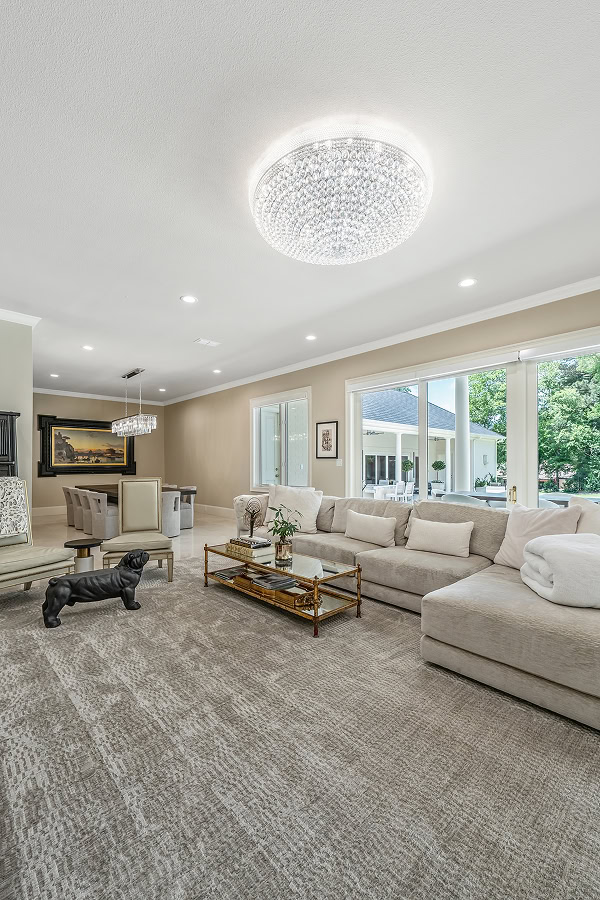 Spacious living room with large windows, modern chandelier, and comfortable seating.