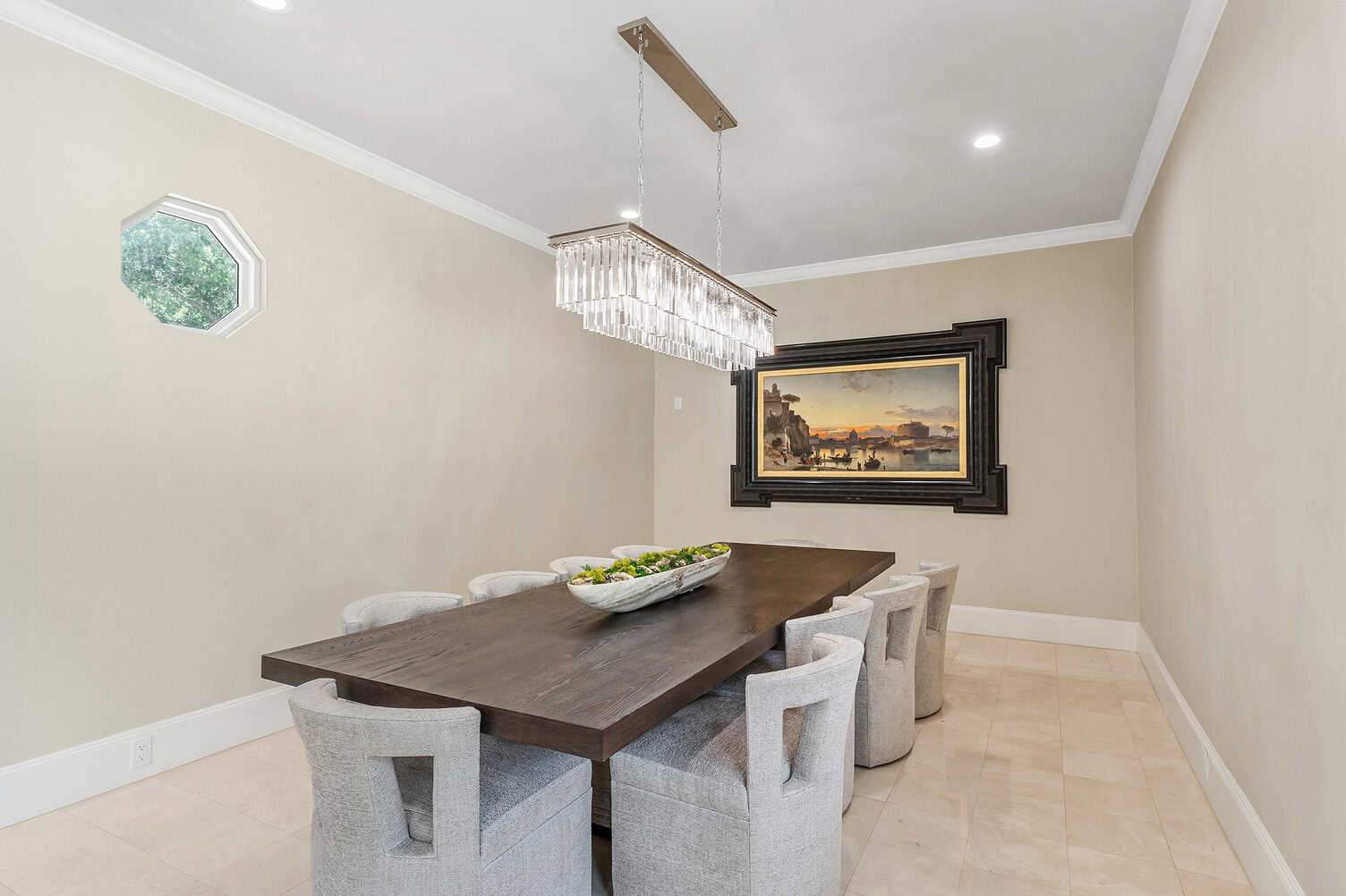 Modern dining room with a large wooden table and eight chairs, chandelier, and landscape painting.