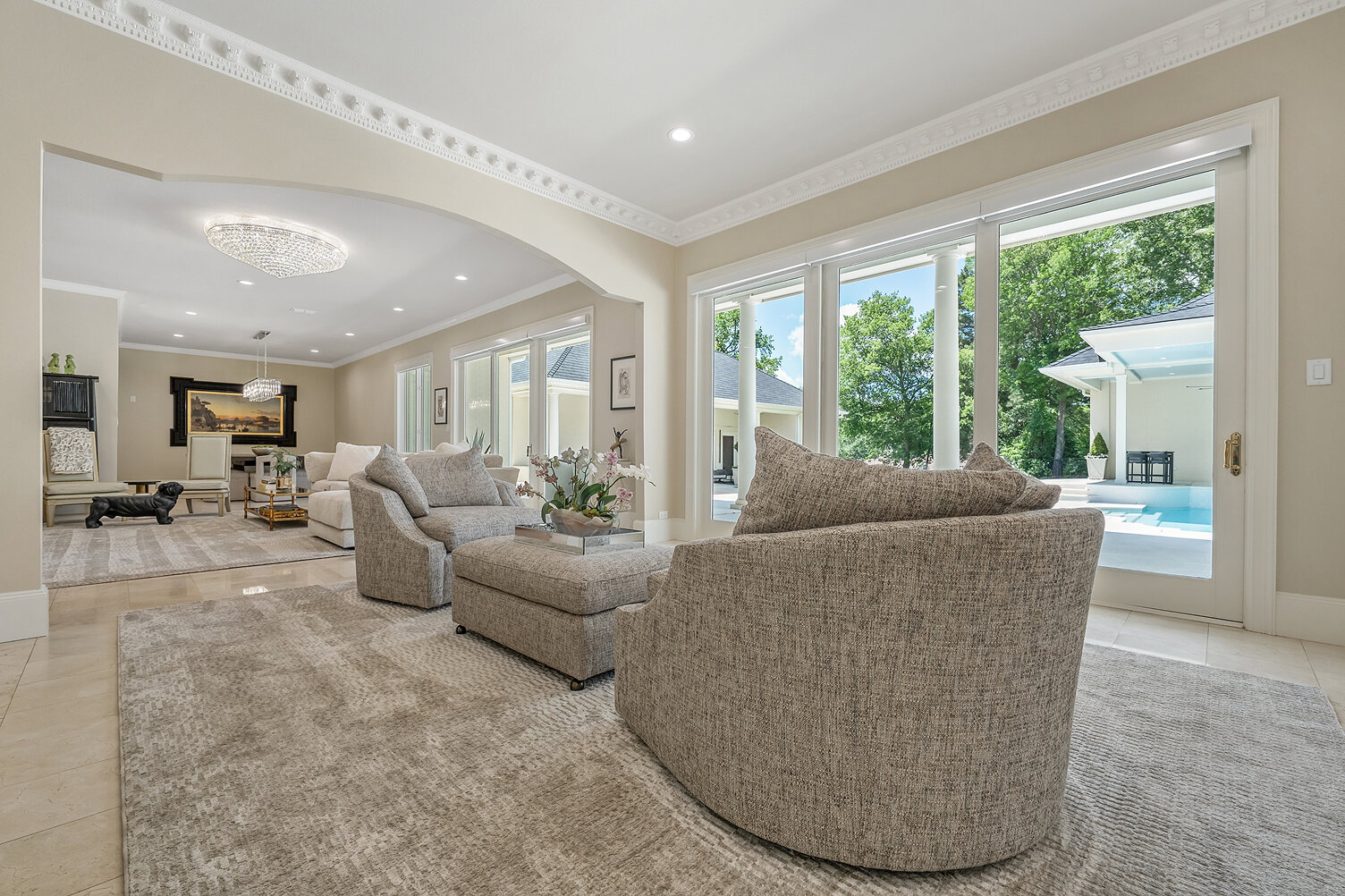 Bright living room with large windows overlooking pool and lush greenery.