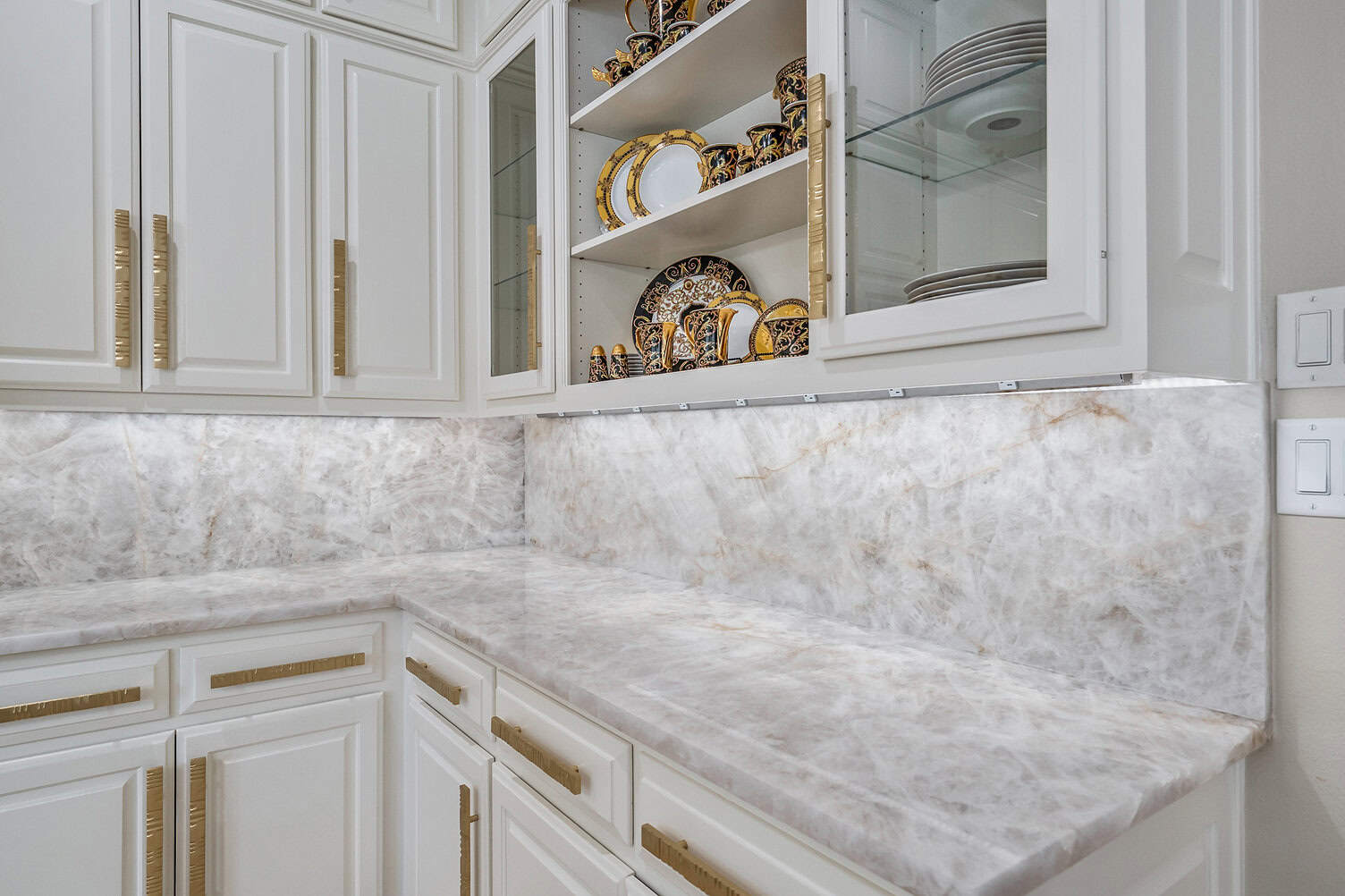 White kitchen cabinets with gold handles and marble countertops.