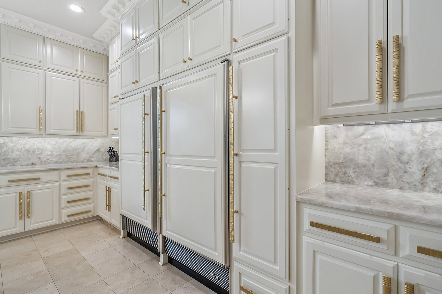 Elegant white kitchen cabinets with gold hardware and marble countertops.