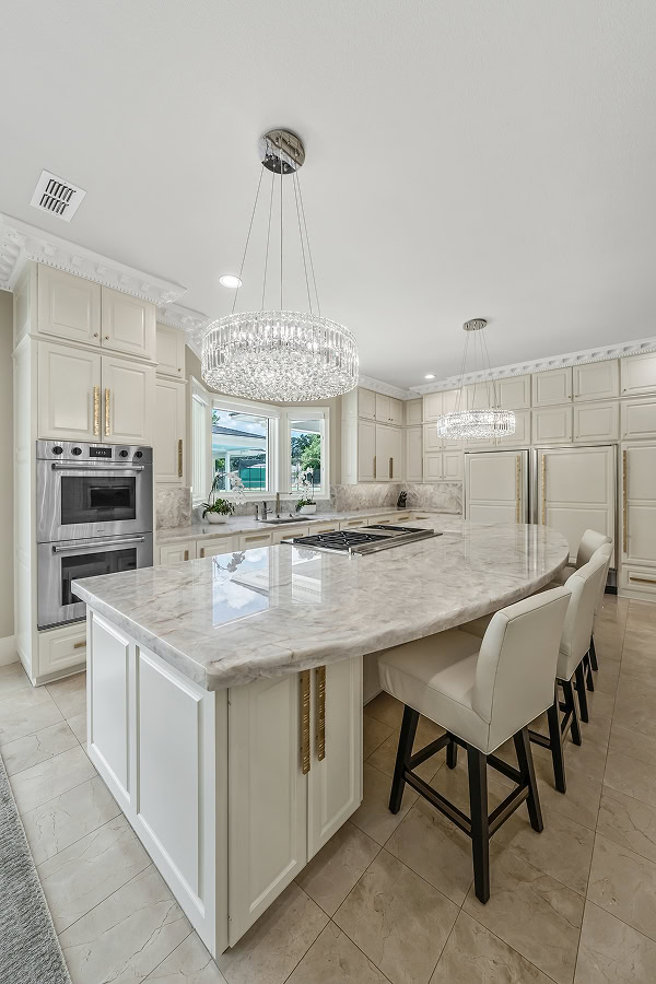 Modern kitchen with marble island, white cabinets, and crystal chandeliers.
