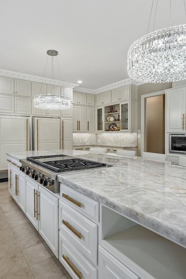 Elegant white kitchen with marble countertops and crystal chandeliers.