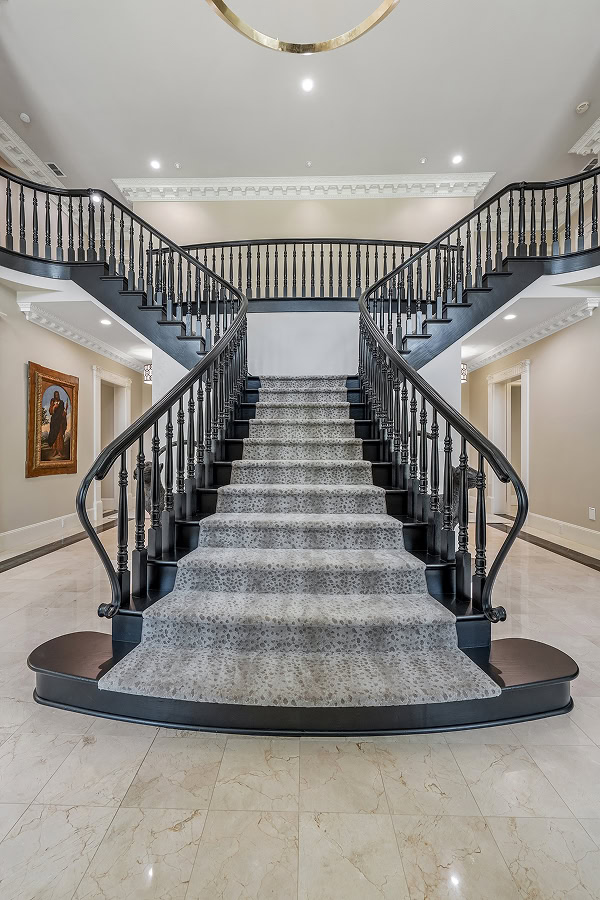 Luxurious double staircase with black railings and gray carpet at The Thornwood.