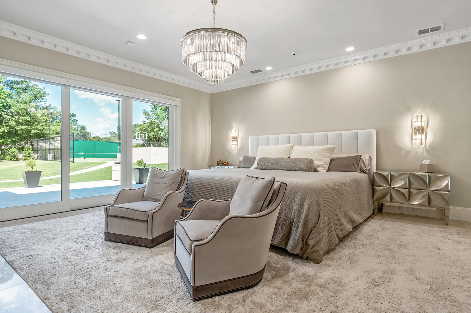 Spacious bedroom with large windows, modern chandelier, and comfortable seating area.