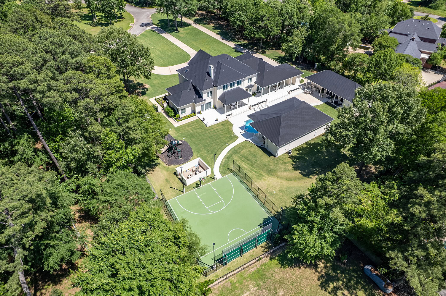 Aerial view of a luxury home with pool, tennis court, and lush greenery.
