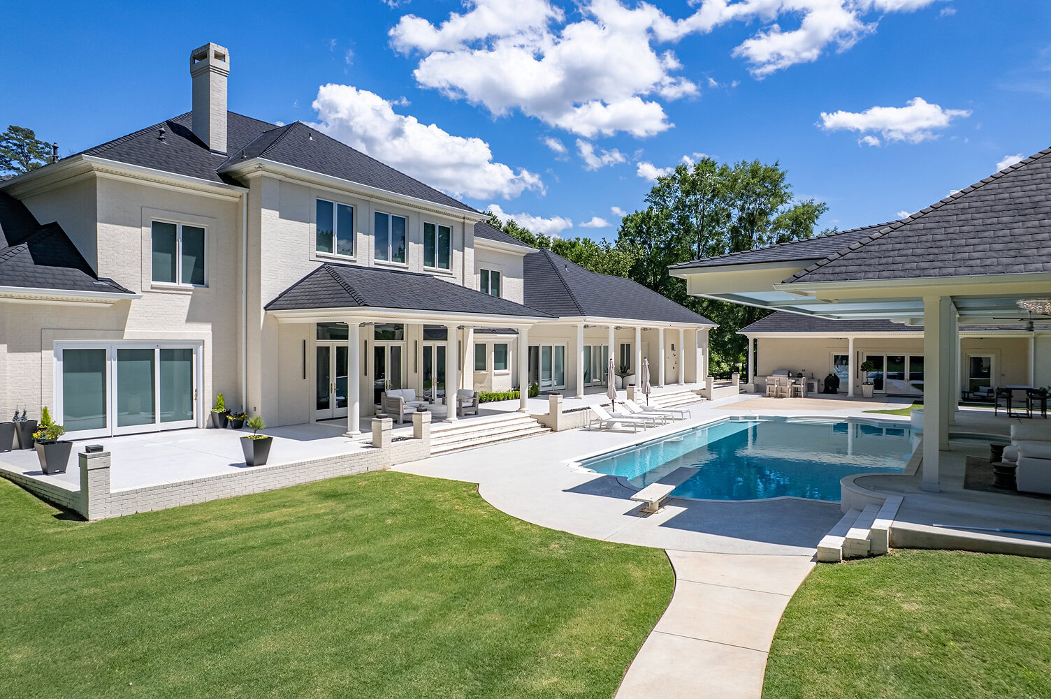Elegant modern house with pool, patio, and lush lawn under blue sky.