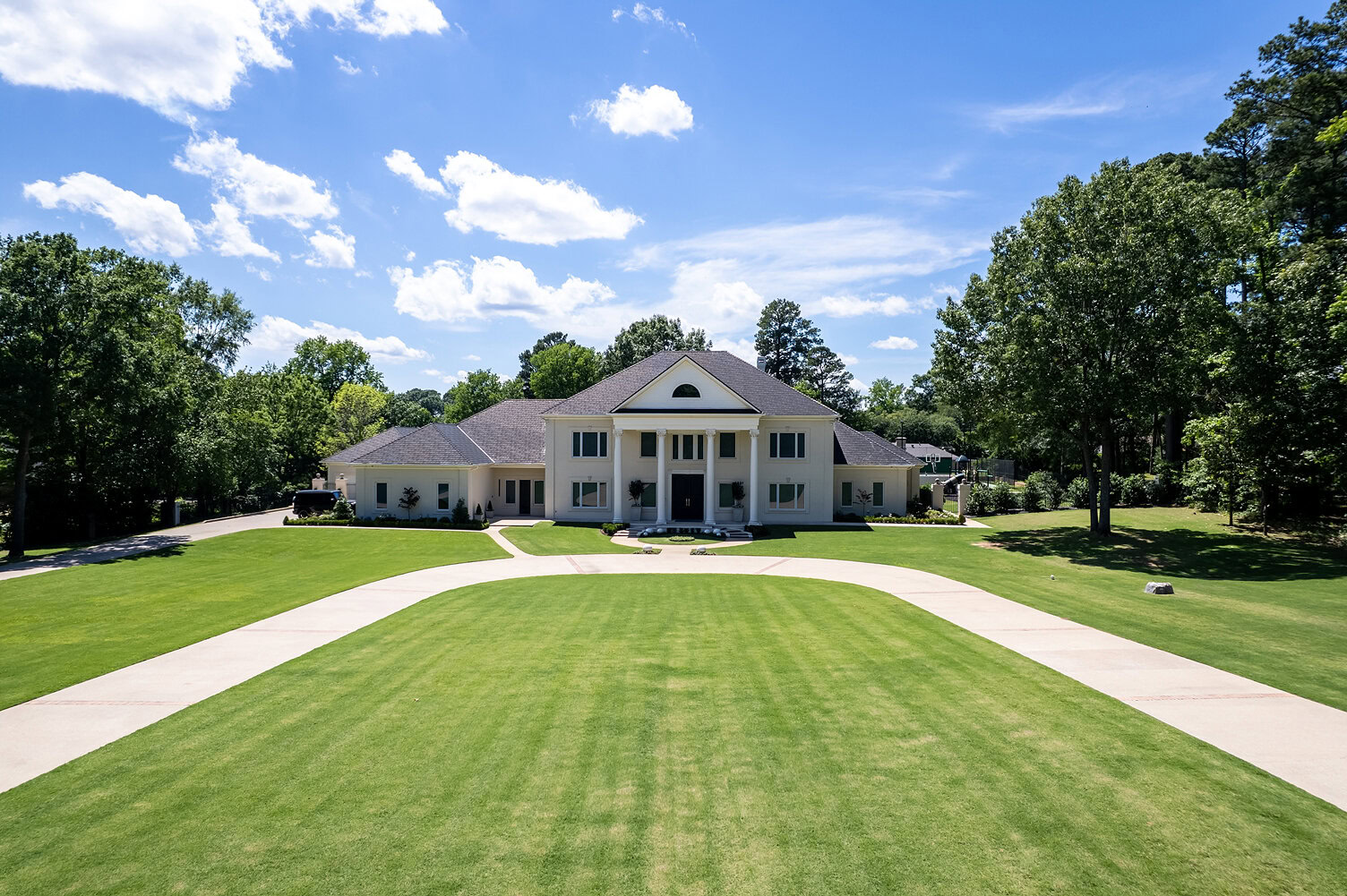 Large white house with columns and manicured lawn under blue sky.