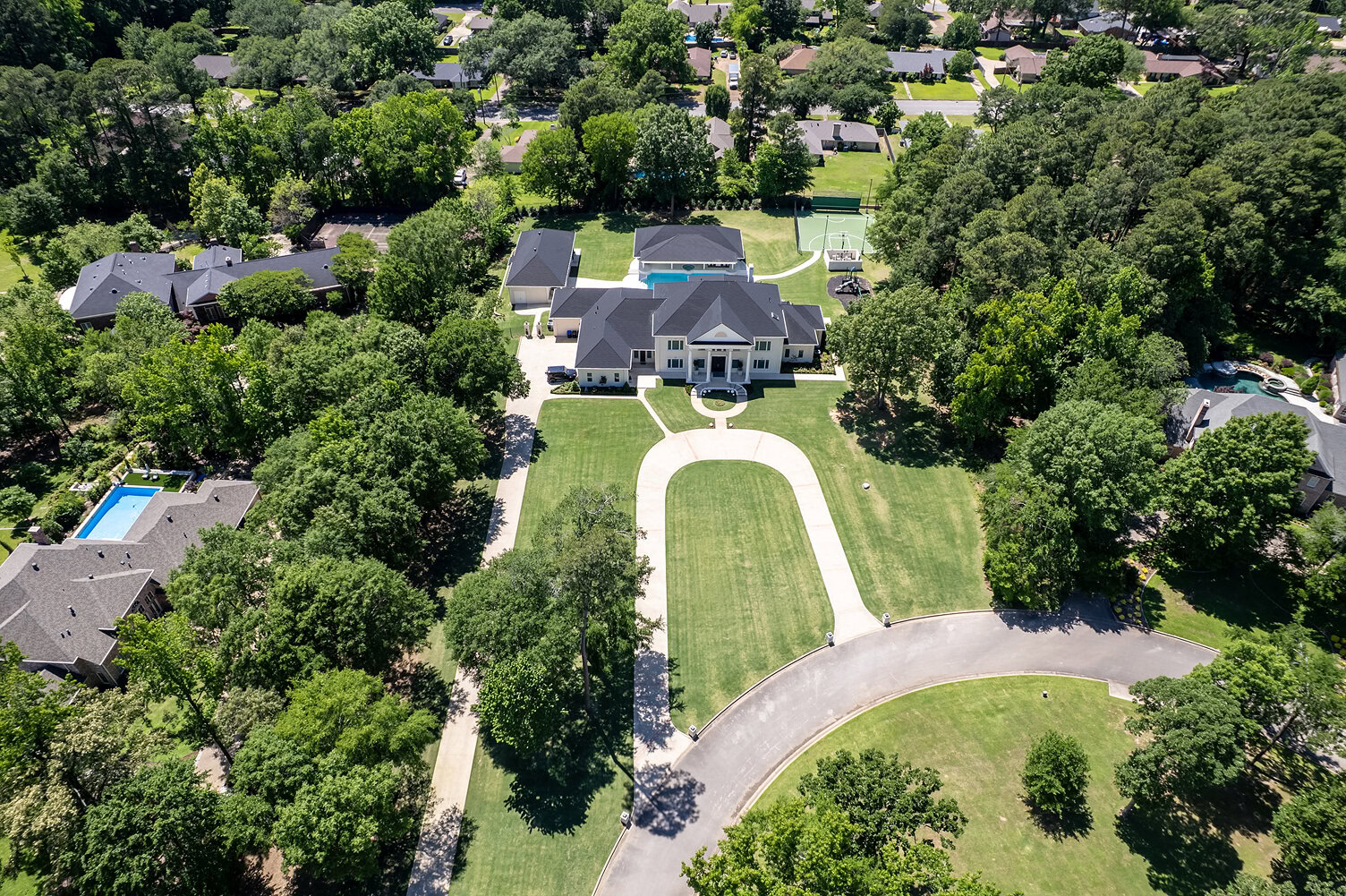 Aerial view of a large luxury estate with expansive lawn and surrounding trees.