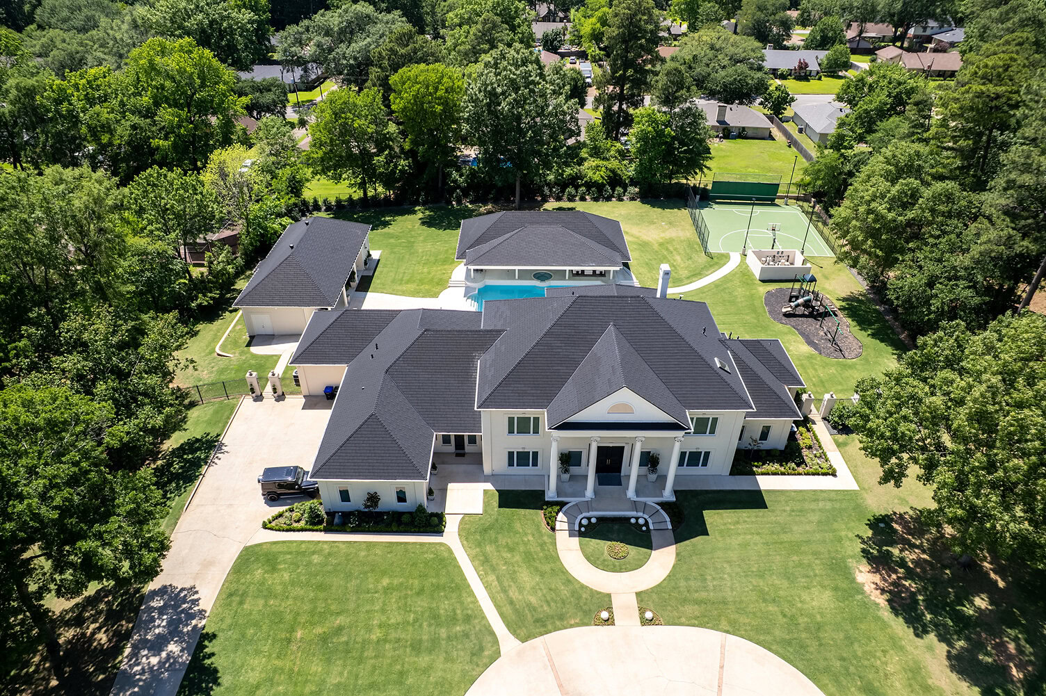 Aerial view of a large luxury house with a pool and tennis court in The Thornwood.