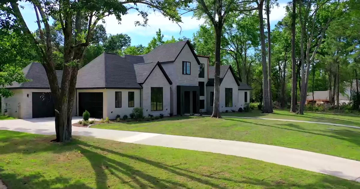 Elegant modern house with large lawn and tall trees in a peaceful neighborhood.